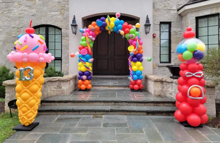Candyland themed birthday balloon arch with ice cream cone and gumball machine sculptures