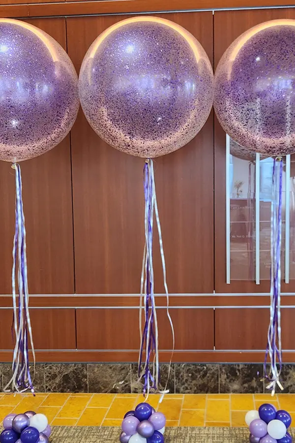 A gorgeous glitter or confetti filled jumbo balloon filled with helium with ribbon or streamers on a base