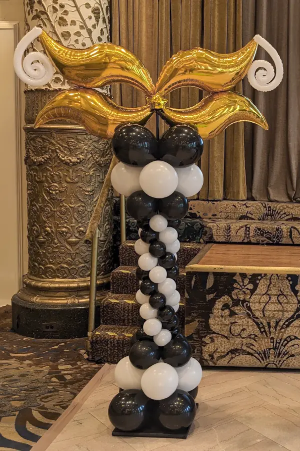 A decorative balloon column topped with foil balloon mask
