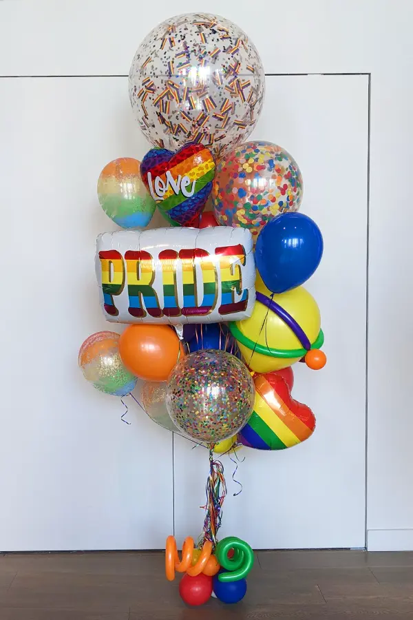 A large balloon bouquet in rainbow colors featuring rainbow foil balloons and confetti balloon accents