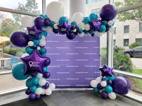 Trendy balloon arch with custom foil balloons with the Women's History Month logo